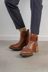 Bota corta de cuero negro con acabado combinado mate y charol. Presenta una tira decorativa con tachas metálicas y hebilla en el tobillo, tacón cuadrado robusto y suela con plataforma.