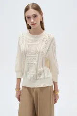 Sweater acrílico en tono natural, de corte holgado, con cuello a la base decorado con sutiles volados, mangas 3/4 y diseño tejido con motivos geométricos calados en el frente.