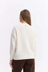 Buzo de punto color blanco, con cuello redondo y diseño de trama combinada con detalles trenzados. Presenta terminaciones tejidas en puños y ruedo.