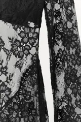 Vestido largo semitransparente confeccionado en tejido de encaje con diseño floral. Presenta escote barco, manga larga y detalle de escote en la espalda con banda cruzada.