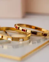 Brazalete rígido dorado con incrustaciones de circonitas rectangulares.