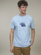 Remera de algodón color celeste, con cuello redondo y manga corta. Presenta un estampado frontal de un diseño botánico en tonos azules y texto.