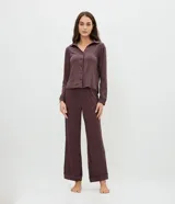 Pijama de dos piezas compuesto por una camisa de manga larga con cuello clásico, cierre frontal de botones y detalle de ribete, y un pantalón largo de corte recto. Ambas prendas presentan un diseño de rayas verticales finas en tono oscuro.