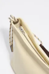Bolso de hombro mediano de piel color beige, con cierre de cremallera, asas de cordón ajustable y logo grabado en el frente.