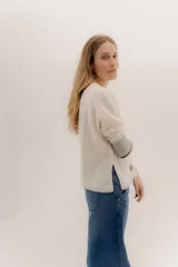 Buzo de punto en color negro con mangas tres cuartos y puños en contraste color marrón. Presenta un diseño holgado con tajos laterales y un aplique circular con logo en la parte inferior.