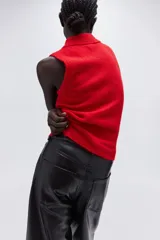 Chaleco corto de punto rojo vibrante, con cuello camisero y tapeta de tres botones oscuros. Presenta un tejido suave y ligeramente texturado, con ribetes acanalados en las sisas y el bajo.