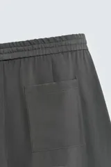 Pantalón de corte relajado, color gris oscuro, con cintura elástica ajustable mediante cordón y pliegues frontales. Presenta bolsillos laterales y bolsillos traseros de parche con pespuntes contrastantes.