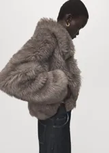 Chaqueta de piel sintética con textura mullida, cuello amplio y cierre frontal, con diseño corto y mangas largas.