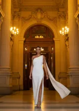 Vestido largo de fiesta confeccionado en crepe satin, con diseño de un solo hombro y tajo lateral profundo. Presenta una capa larga que nace del hombro y cae con fluidez.