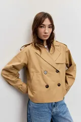 Cazadora corta de estilo gabardina en color tostado, con diseño cruzado de doble botonadura, solapas amplias, mangas largas con trabillas en los puños y hombreras.
