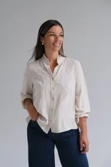 Blusa de lino color beige con cuello mao y detalles de volados sutiles. Presenta bordados florales en color blanco en el frente y mangas largas con puños elásticos.