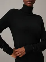 Vestido negro de lana merina, corte recto, largo hasta la rodilla, cuello alto y mangas largas.
