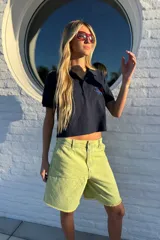 Remera tipo polo color amarillo pálido, de algodón, con cuello clásico y mangas cortas. Presenta un bordado de una rosa azul en el pecho.