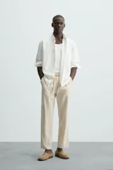 Pantalón de corte relajado color beige confeccionado en tejido de mezcla de algodón y lino. Posee cintura elástica ajustable con cordón, bolsillos frontales y bolsillos traseros de vivo.