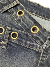 Short de denim tiro bajo con diseño cruzado en la cintura, efecto desgastado y detalles de ojalillos metálicos dorados.