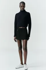 Falda pantalón de tiro medio en color blanco, con diseño minimalista y detalle de cinturón fino integrado con hebilla metálica. Cuenta con cierre lateral mediante cremallera oculta.