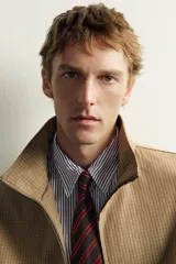 Cazadora regular fit de la colección Aaron Levine x ZARA, confeccionada en tejido con mezcla de algodón con patrón de cuadros pequeños en tonos beige y marrón. Cuenta con cuello subido, manga larga con puño ajustable con botón a presión, bolsillos de vivo en la cadera, bajo ajustable con elástico en los laterales y cierre frontal con cremallera.