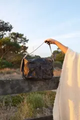 Bolso de hombro tipo hobo con textura de cuero grabado tipo cocodrilo, color marrón oscuro. Cuenta con dos bolsillos frontales con solapa y cierre, y una correa ajustable.