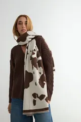 Bufanda rectangular de tejido de punto, con diseño estampado de manchas abstractas en color mostaza sobre fondo crudo y terminación con flecos cortos.