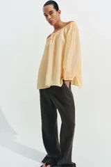 Blusa de lino color amarillo pastel, con escote recto ajustable mediante lazadas, hombros descubiertos y mangas largas abullonadas con puños elásticos.