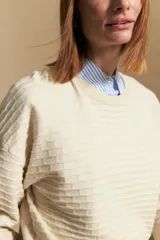 Sweater color crema con mangas abullonadas y puños elastizados. Presenta una textura tejida en relieve con patrón de ladrillos en el cuerpo y rayas horizontales en las mangas.