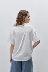 Remera color tostado de corte holgado, con cuello redondo y mangas cortas. Presenta un estampado gráfico frontal de estilo veraniego con ilustraciones de una langosta, conchas, limón, una copa y la inscripción 'Summer Club'.