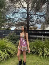 Vestido corto de tela metalizada en tono fucsia con reflejos dorados, con escote en V, diseño de top con triángulos, aberturas laterales en la cintura y doble volado irregular en el ruedo.