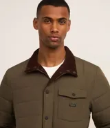 Campera puffer negra con cuello alto, cierre frontal con botones a presión, bolsillos laterales y un bolsillo cargo en el pecho. Presenta un diseño acolchado y forro interior suave.