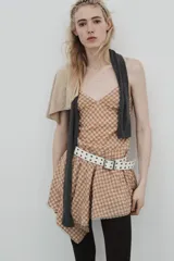 Vestido corto con escote en V y tirantes finos ajustables, confeccionado en tejido a cuadros beige y rojo. La falda es asimétrica y presenta un bajo con detalle de encaje.