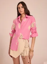 Camisa rosada de manga larga con cuello clásico y cierre frontal con botones. Presenta bordados de encaje color crema en forma de paisley en la parte superior delantera y en las mangas.