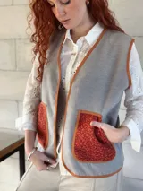 Chaleco gris de paño con bolsillos delanteros de tejido rústico color ladrillo y ribete color ocre. Diseño holgado.