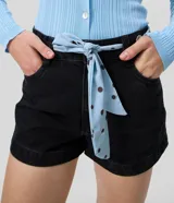 Short de jean negro de tiro alto con bolsillos delanteros y traseros, cierre con botón y cremallera, e incluye un pañuelo celeste con lunares y ojales metálicos para usar como lazo en la cintura.