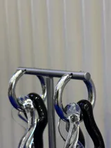 Aros colgantes de diseño irregular, compuestos por una argolla metálica plateada y dos piezas de vidrio soplado entrelazadas en colores negro y transparente.