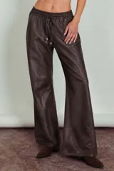Pantalón de cuero color chocolate con corte recto y holgado. Presenta cintura elástica con cordón ajustable y costuras horizontales en la parte inferior de las piernas.
