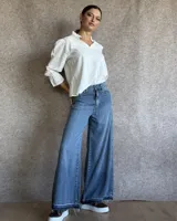Pantalón de jean azul de tiro medio, con corte wide leg y ruedo deshilachado.