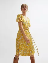 Vestido midi cruzado de color ocre con diseño floral estampado, escote en V y mangas cortas con vuelo. Cuenta con un lazo ajustable en la cintura.