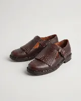 Mocasín de cuero natural color marrón, con costuras visibles, hebilla lateral metálica y solapa desmontable con flecos.