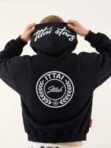 Hoodie negro con capucha, diseño estampado en la espalda con el logo de la marca dentro de un círculo de laureles y texto en la parte posterior de la capucha.