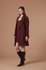 Saco largo tipo trench de color tostado, con diseño de doble botonadura, solapas clásicas y cinturón ajustable en la cintura. Presenta mangas largas con trabillas en los puños y una silueta estructurada y fluida.