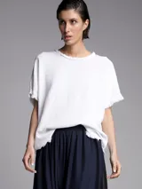 Remera blanca de corte holgado con cuello redondo y flecos en las mangas y el ruedo.