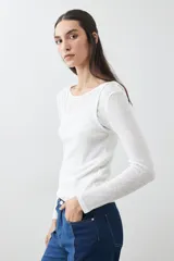 Remera de manga larga, color blanco roto, con cuello bote y textura acanalada. Presenta un efecto de doble capa o transparencia sutil en el escote.