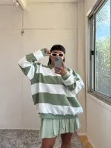 Buzo de corte oversize con diseño de rayas horizontales anchas en color verde y crudo. Presenta cuello redondo, mangas largas y puños elásticos, confeccionado en tela con interior de felpa.