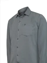 Camisa de manga larga color gris, confeccionada en una mezcla de tencel y lino. Presenta cuello clásico, cierre frontal con botones, puños abotonados y un bolsillo en el pecho con el logo de la marca bordado.