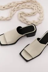 Sandalia de cuero vacuno color marrón oscuro, con faja ancha y punta cuadrada. Presenta talón abierto y taco bajo y grueso.