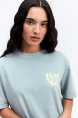 Remera de corte oversize color verde agua con efecto acid wash, cuello redondo y estampa pequeña en el pecho. Presenta una silueta relajada y mangas cortas.