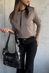 Remera de manga larga con diseño a rayas horizontales en color beige y negro, confeccionada en tejido de punto acanalado. Presenta un cuello redondo con un detalle de cordón fino negro que cae hacia el pecho.