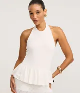 Top blanco de tejido piquet texturizado, con cuello halter y peplum con volado en la cintura.
