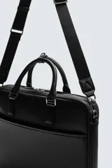 Maletín negro con textura grabada, diseño estructurado y asas de mano. Cuenta con cierre principal de cremallera, bolsillo frontal plano y bolsillo interior para dispositivos electrónicos de hasta 13 pulgadas. Incluye asa de hombro ajustable y extraíble.