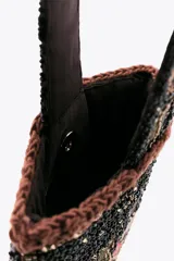 Bolso pequeño de mano con asa corta, confeccionado con abalorios negros y diseño floral bordado en tonos rosa y verde. Presenta flecos largos de abalorios en la parte inferior y cierre con botón a presión.