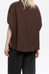 Camisa marrón de corte capa confeccionada en tejido de caída fluida. Presenta cuello camisero, cierre frontal con botones y mangas cortas tipo murciélago con pliegues.